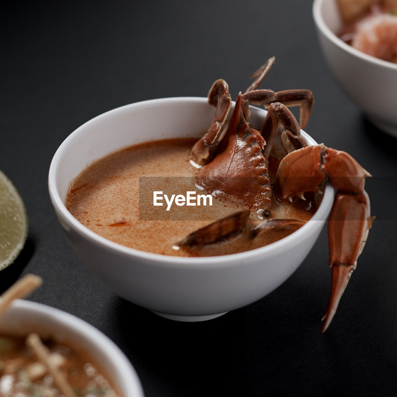 High angle of yummy whole boiled crab lying in tasty spicy tomato gravy in white ceramic bowl on gray table among other aromatic colorful dishes in modern restaurant