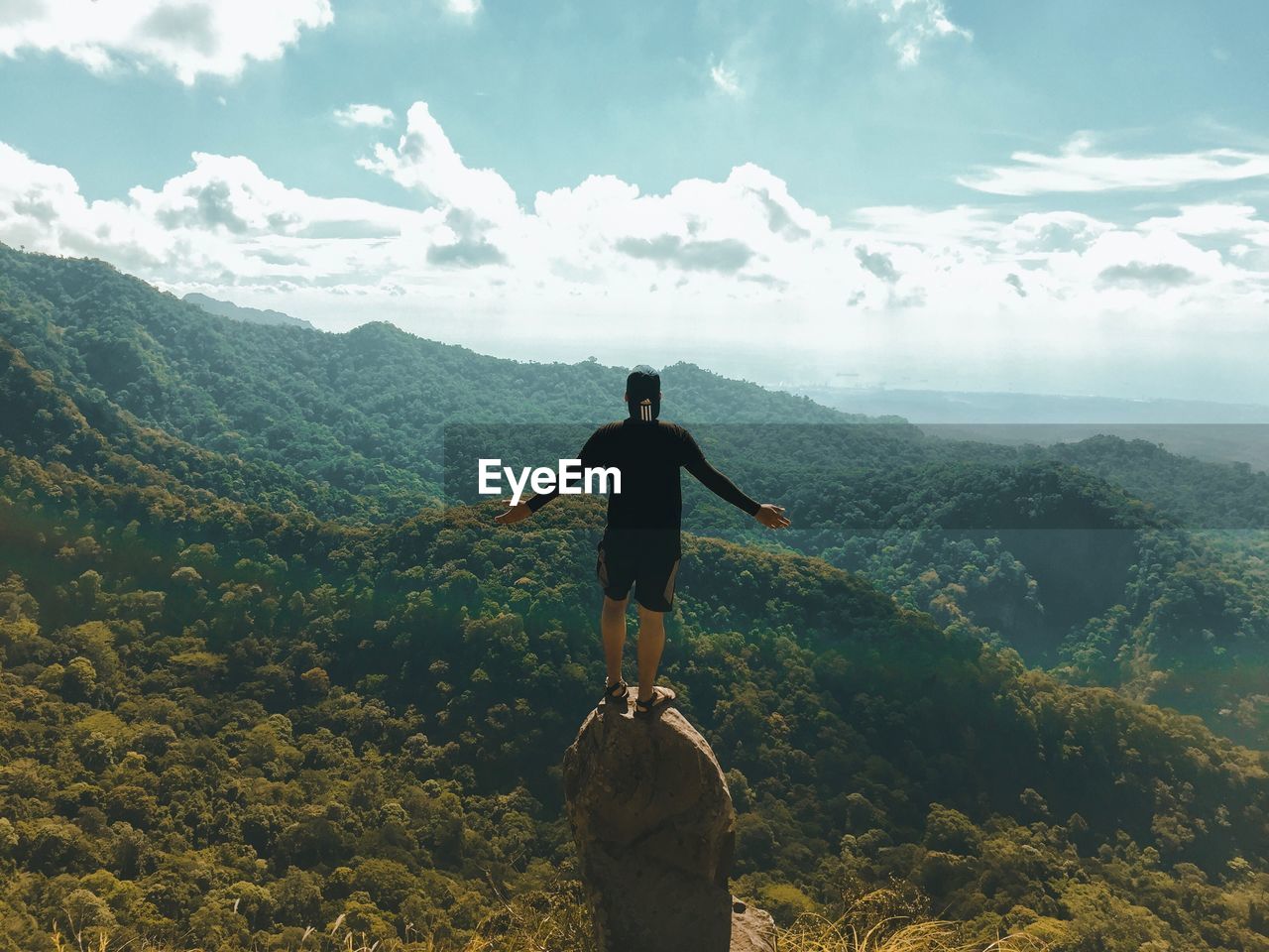 Rear view of man with arms outstretched standing on rock