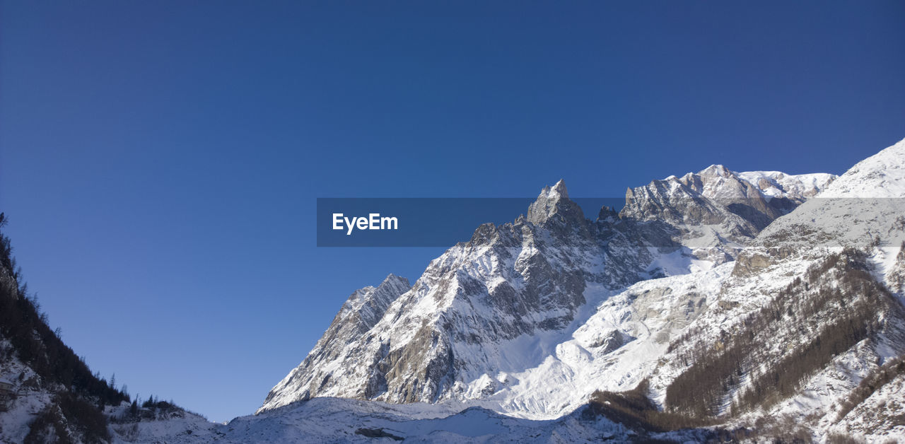 Low angle view of snowcapped mountains against clear blue sky