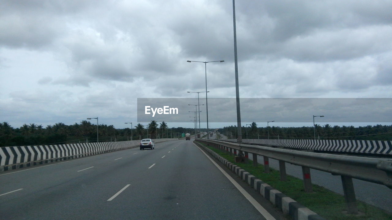 CARS ON ROAD AGAINST CLOUDY SKY