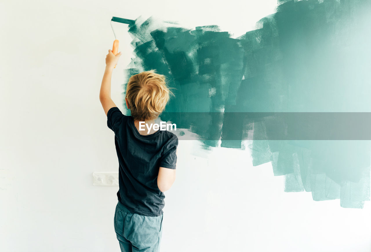 Rear view of boy painting on wall at home