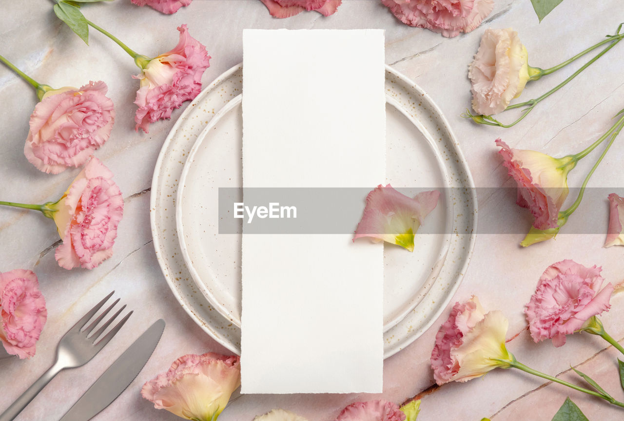 Wedding menu laying on a ceramic plate on a marble table decorated with flowers and ribbons