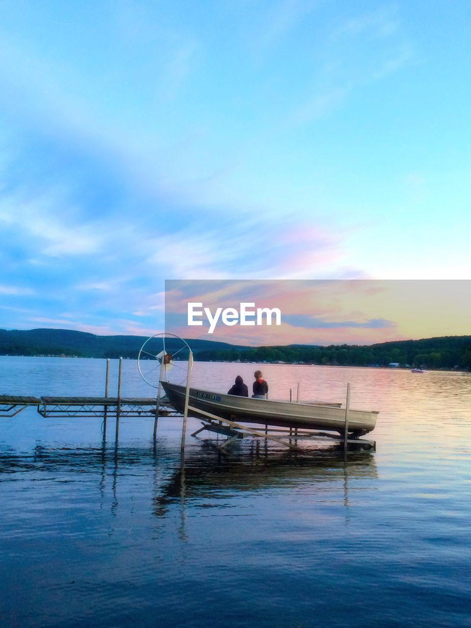 Rear view of children on pier over lake against dramatic sky during sunset