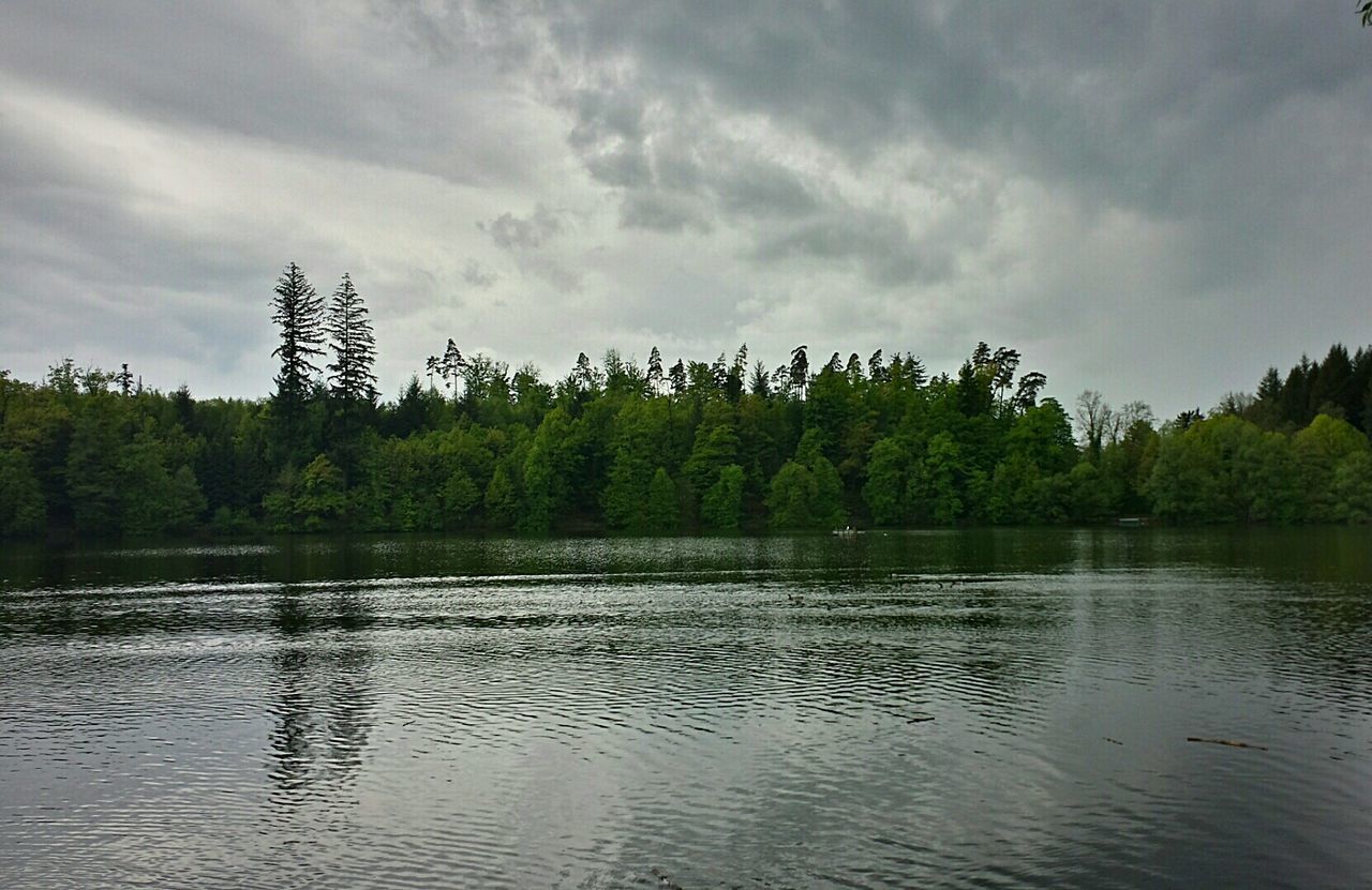 Calm river with trees in distance against clouds