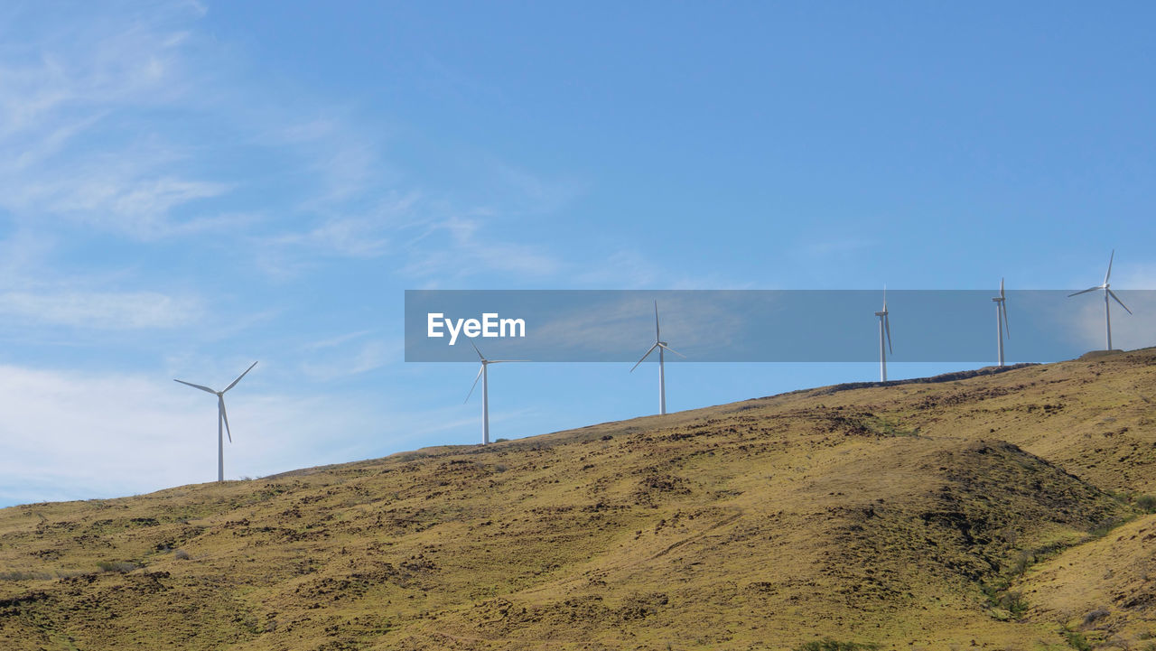 WINDMILLS ON FIELD AGAINST SKY