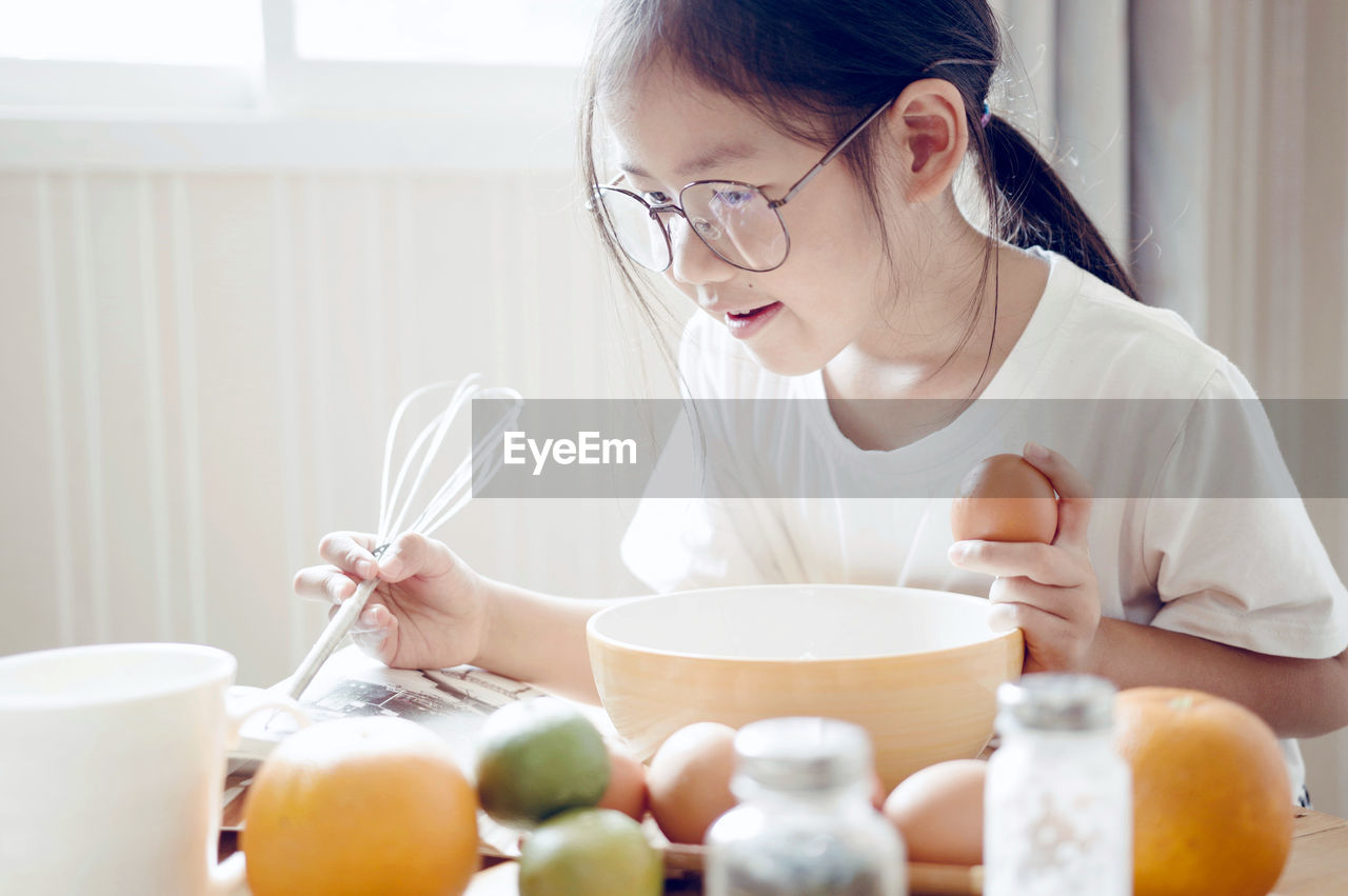 Girl reading book while preparing food at home