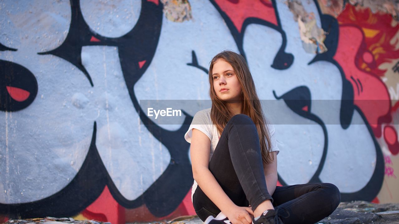 Full length of teenage girl sitting against graffiti wall