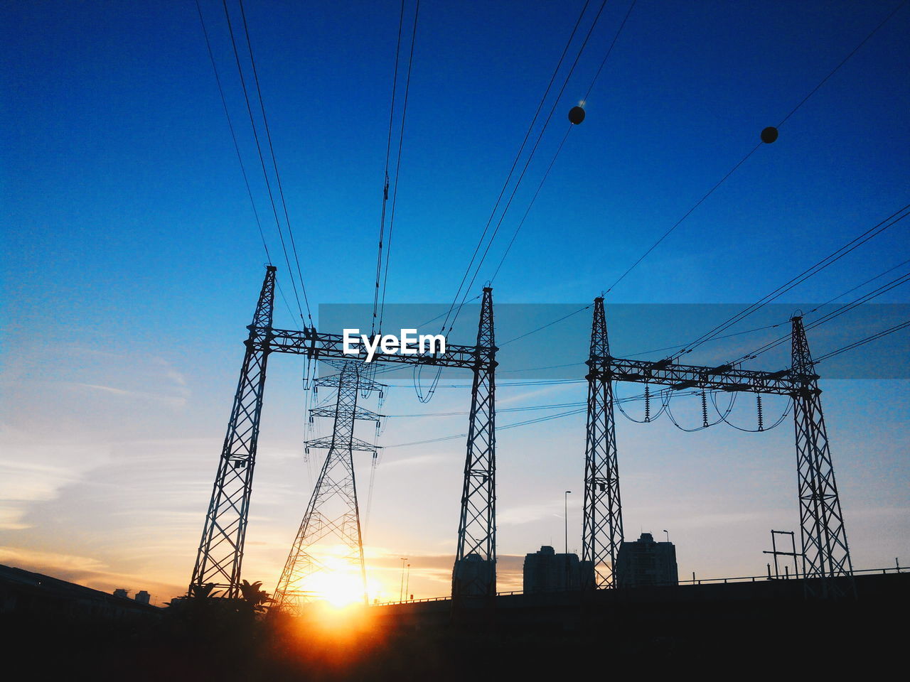 Silhouette electricity pylon against blue sky during sunset