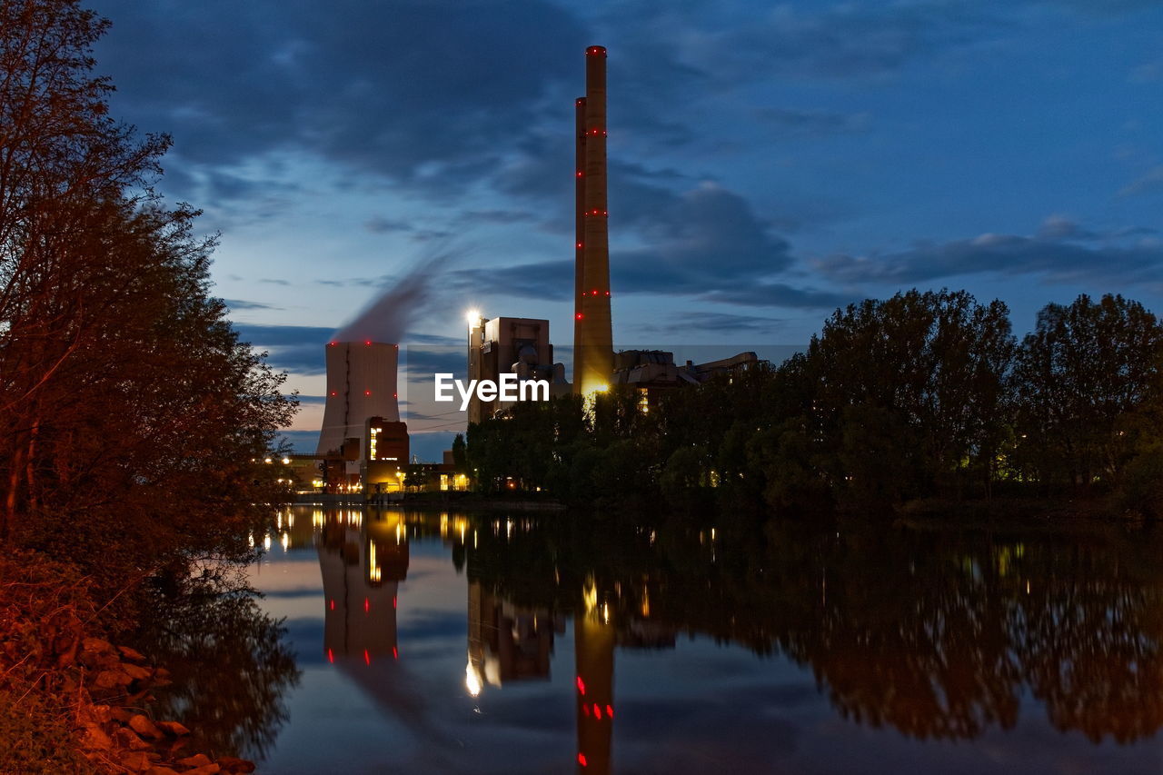 Panoramic view of factory by lake against sky