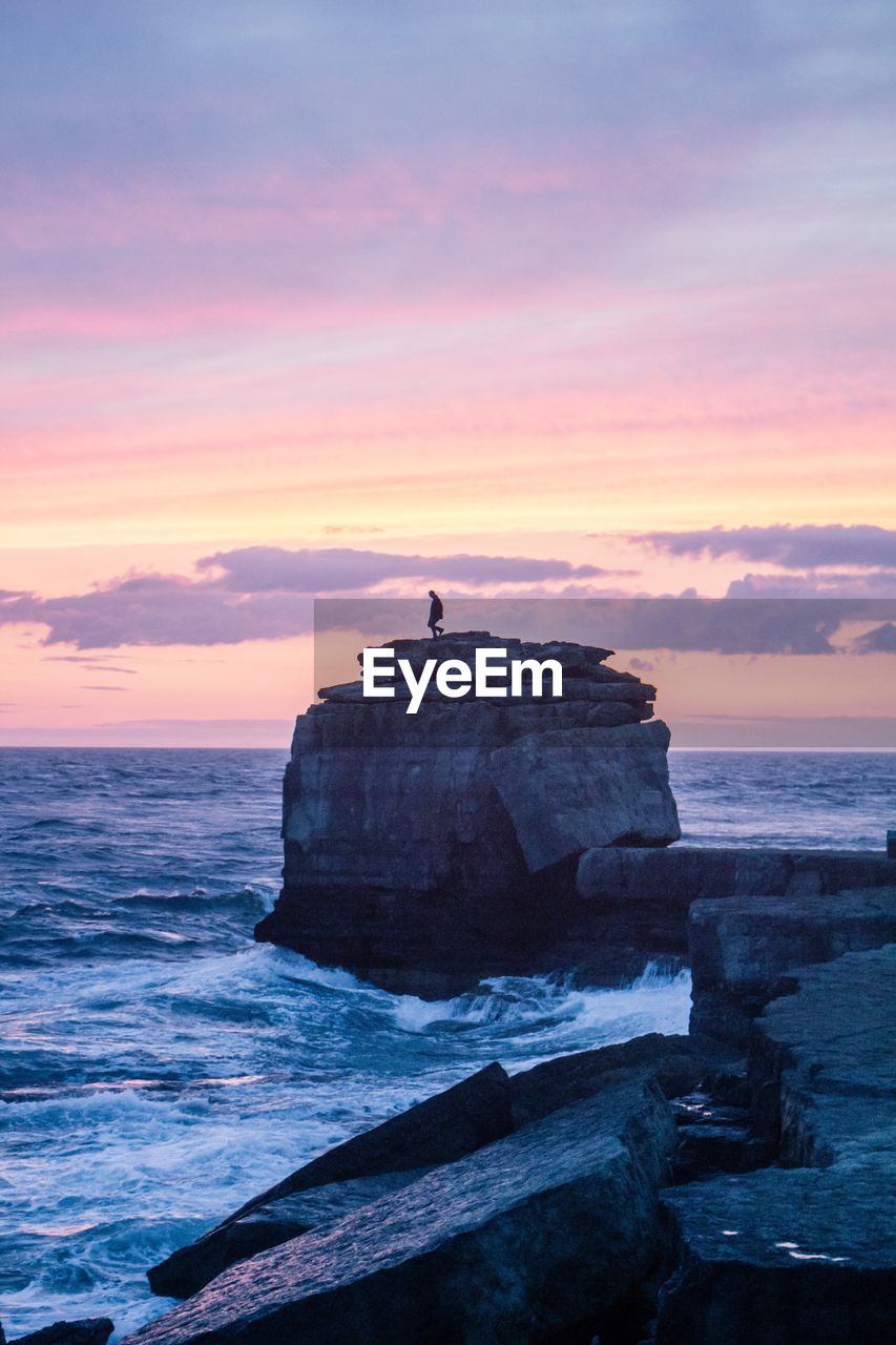 Distant view of silhouette person on cliff by sea against sky