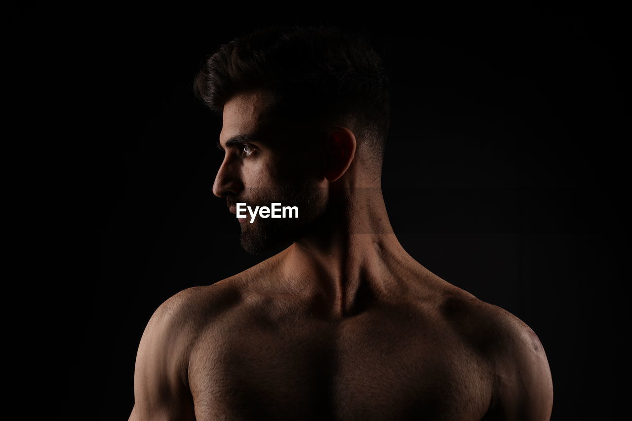 low angle view of shirtless man standing against black background