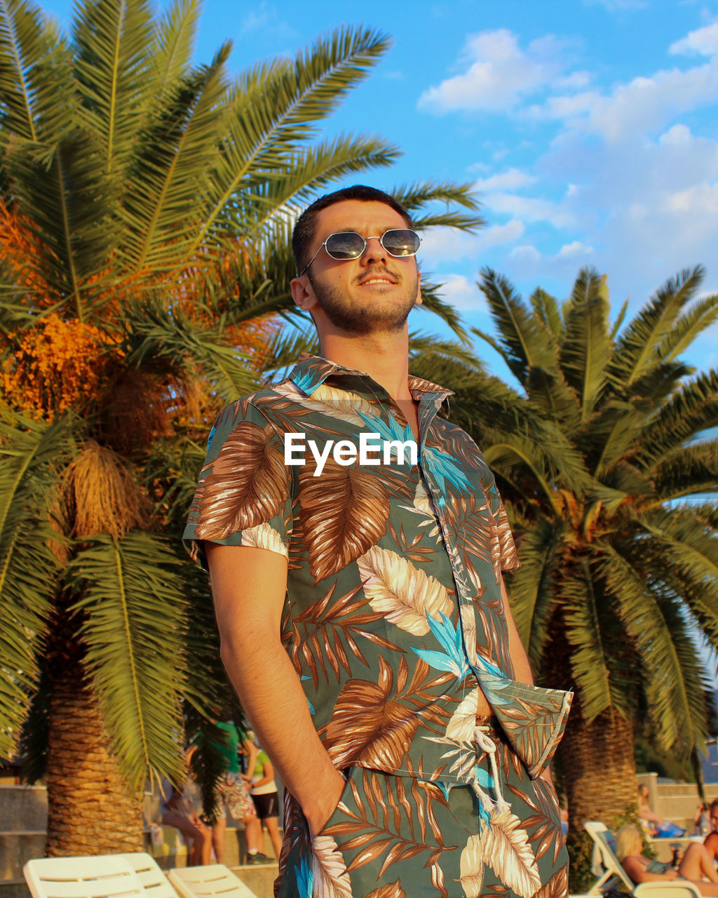 Low angle view of man wearing sunglasses standing against palm trees