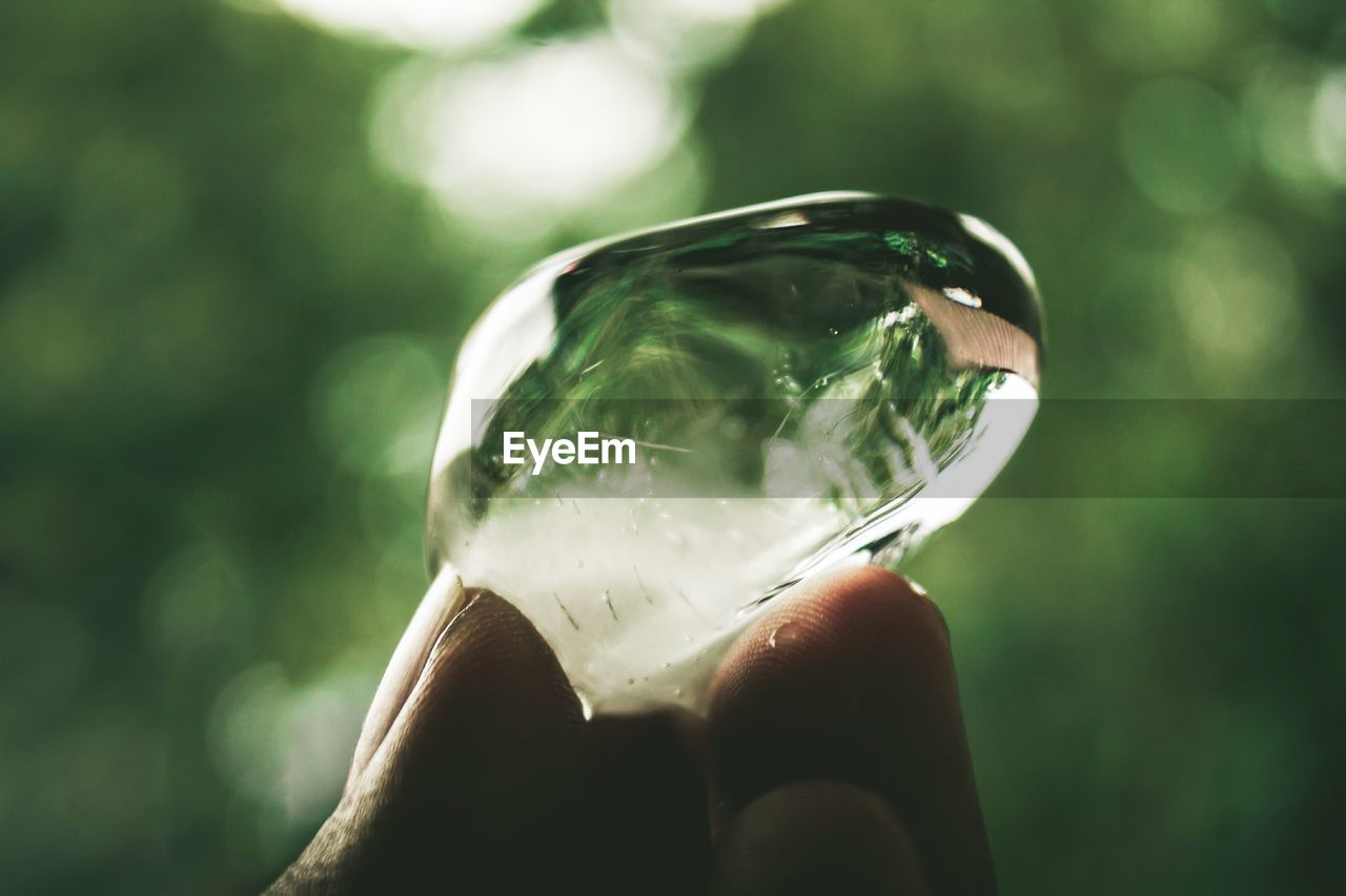 CLOSE-UP OF HAND HOLDING GLASS OF BLURRED