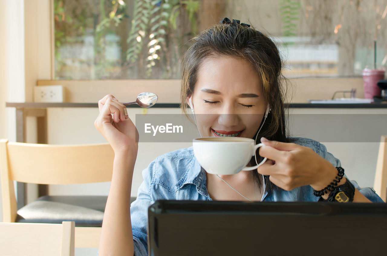 Smiling young woman drinking coffee in cafe