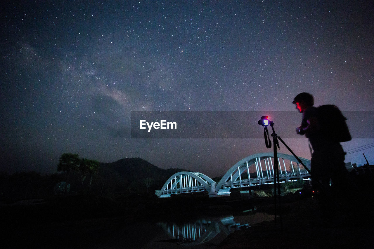 Man photographing on camera against sky at night