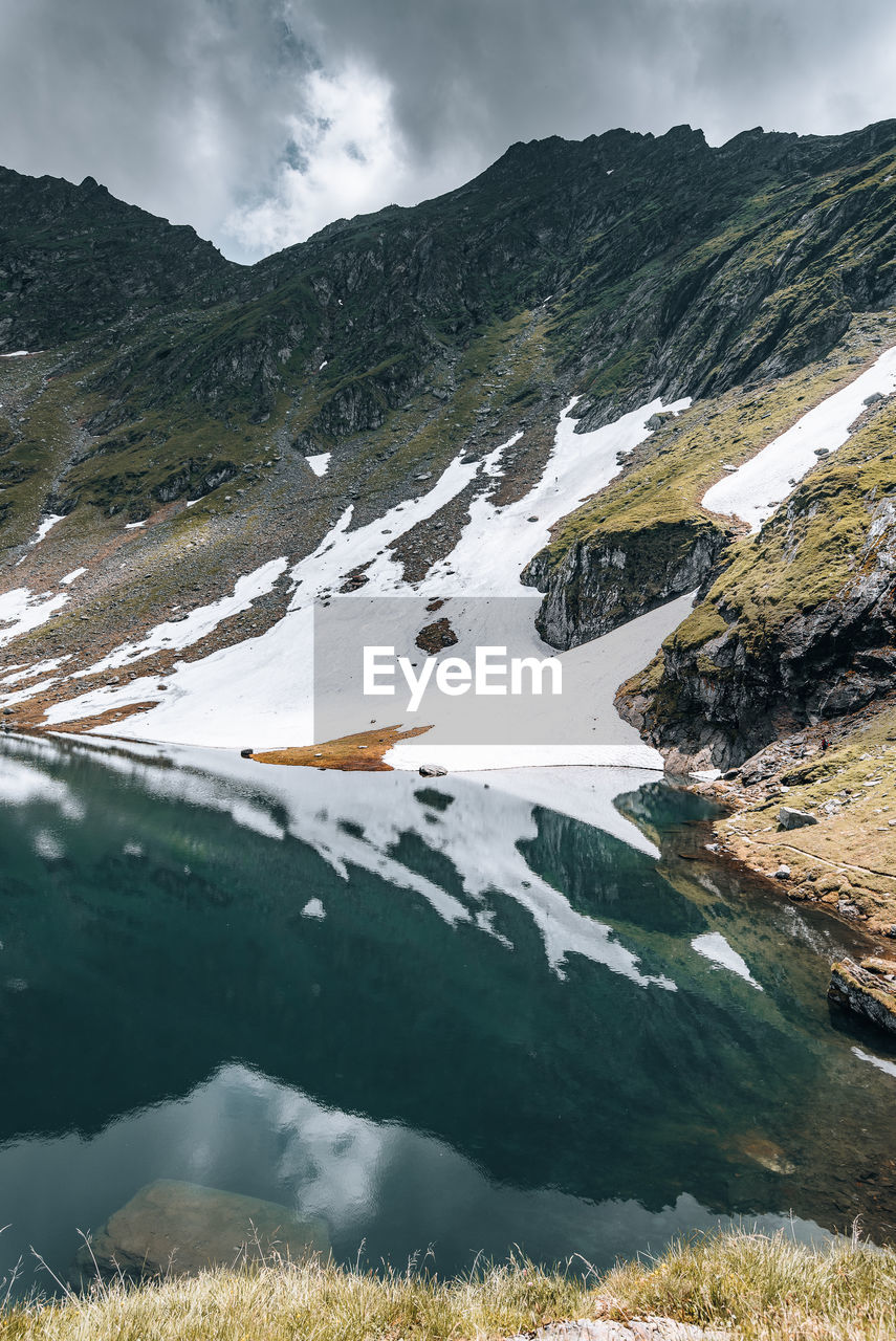 Snow patches on mountain ridge  with lake and reflection