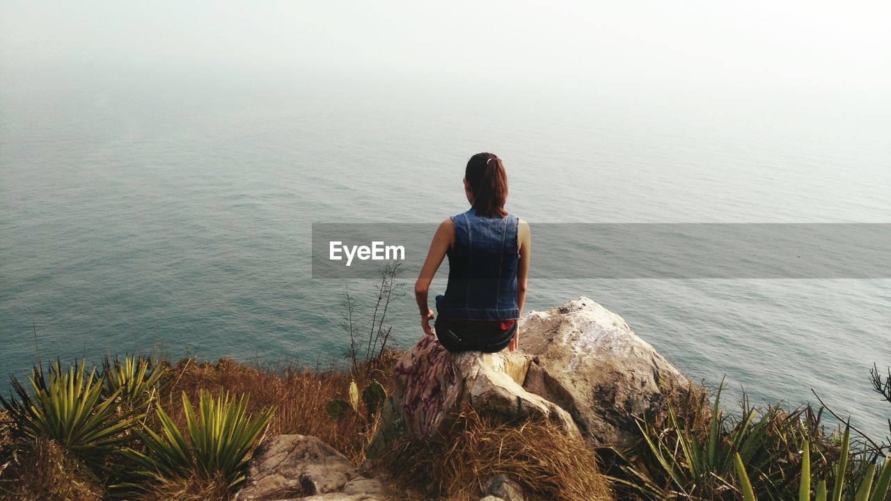 Rear view of person sitting on rocks next to lake