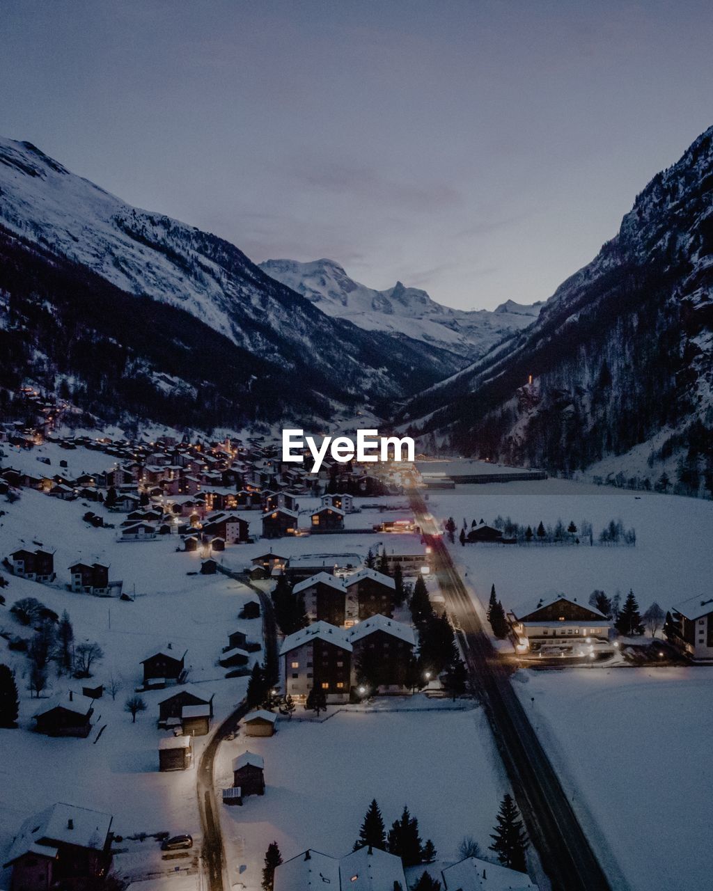 Aerial shot of town surrounded by snowcapped mountains at dusk during winter