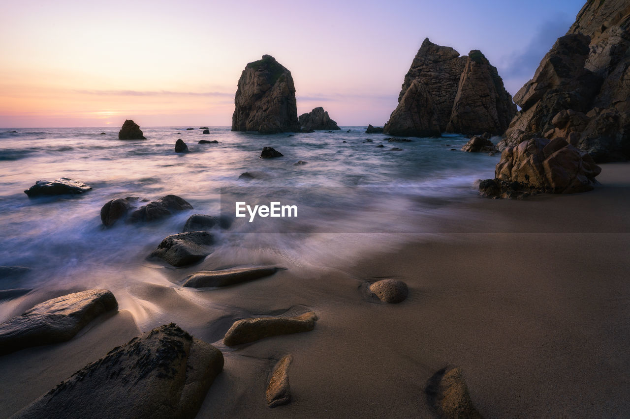 Rocks on beach against sky during sunset