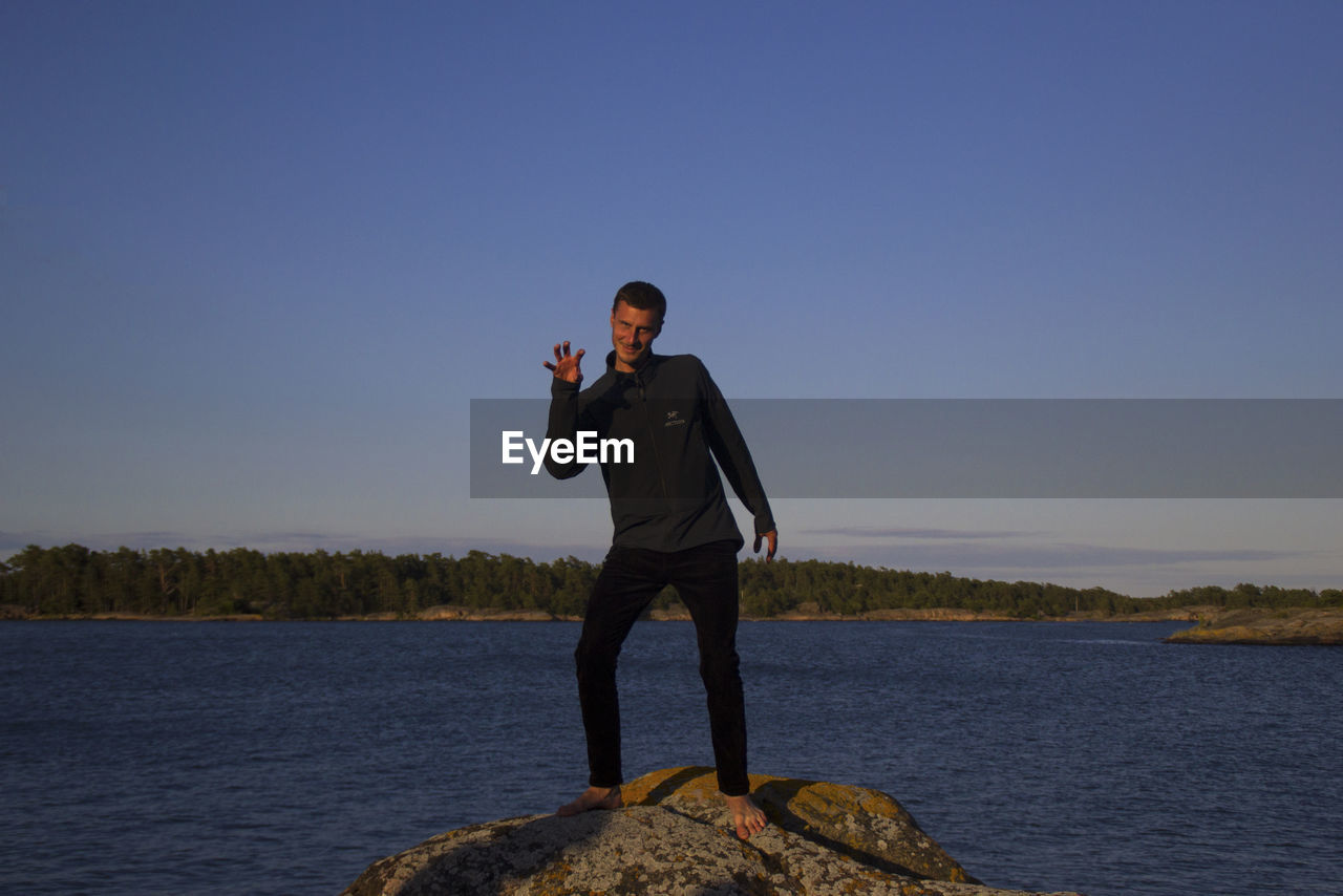 Man gesturing while standing on rock by sea against sky