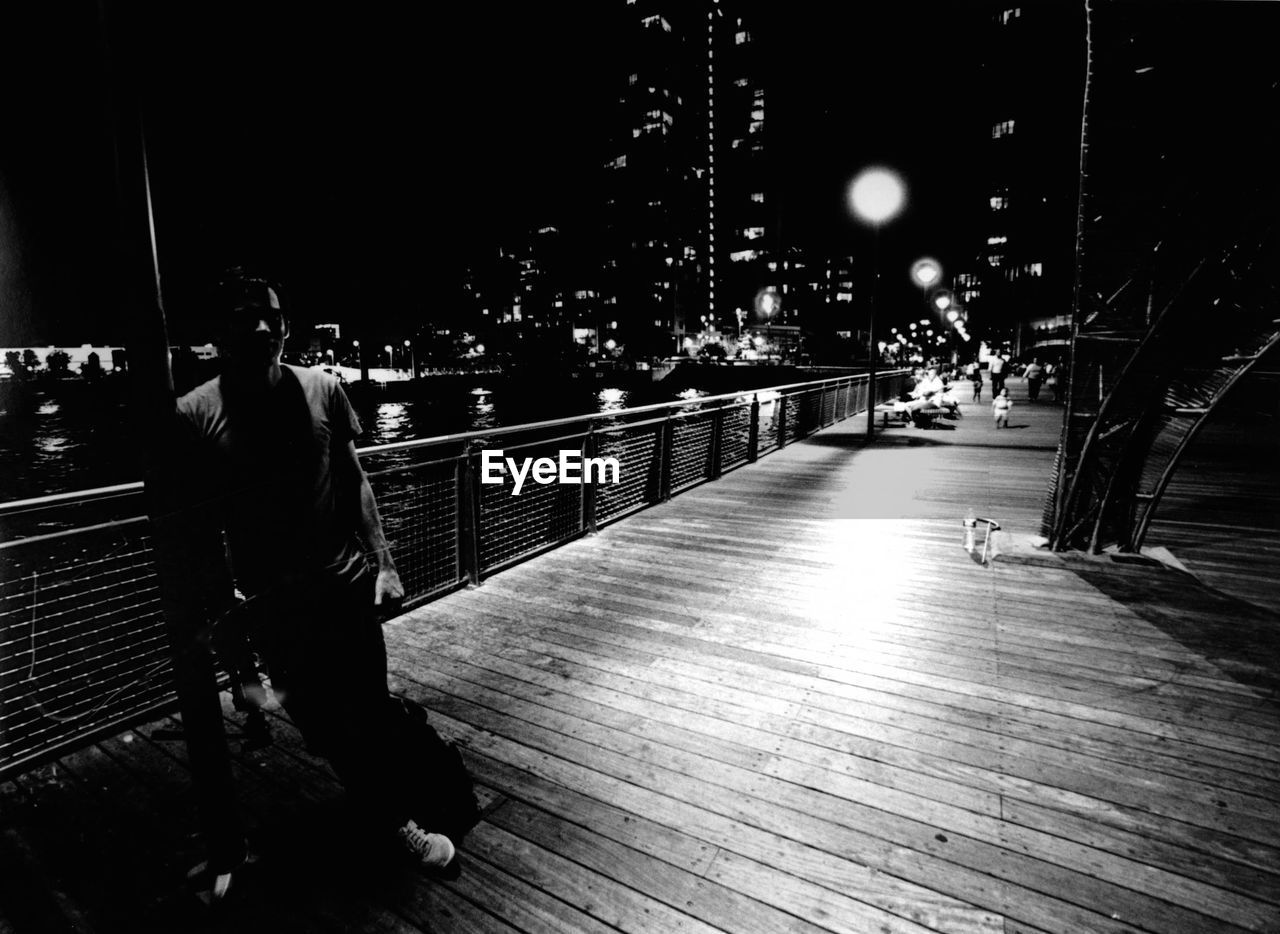 Man standing on pier against calm river at night