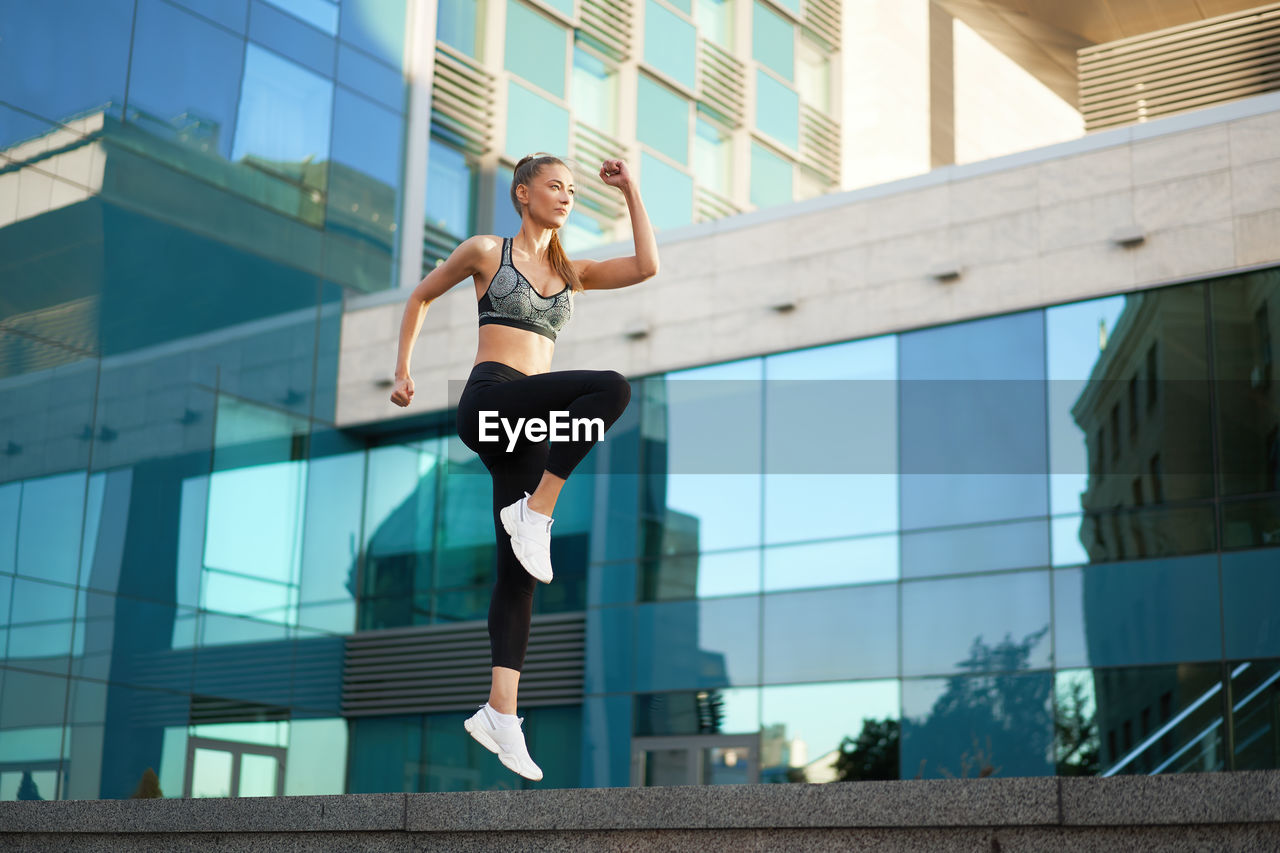 Full length of young woman jumping against glass wall