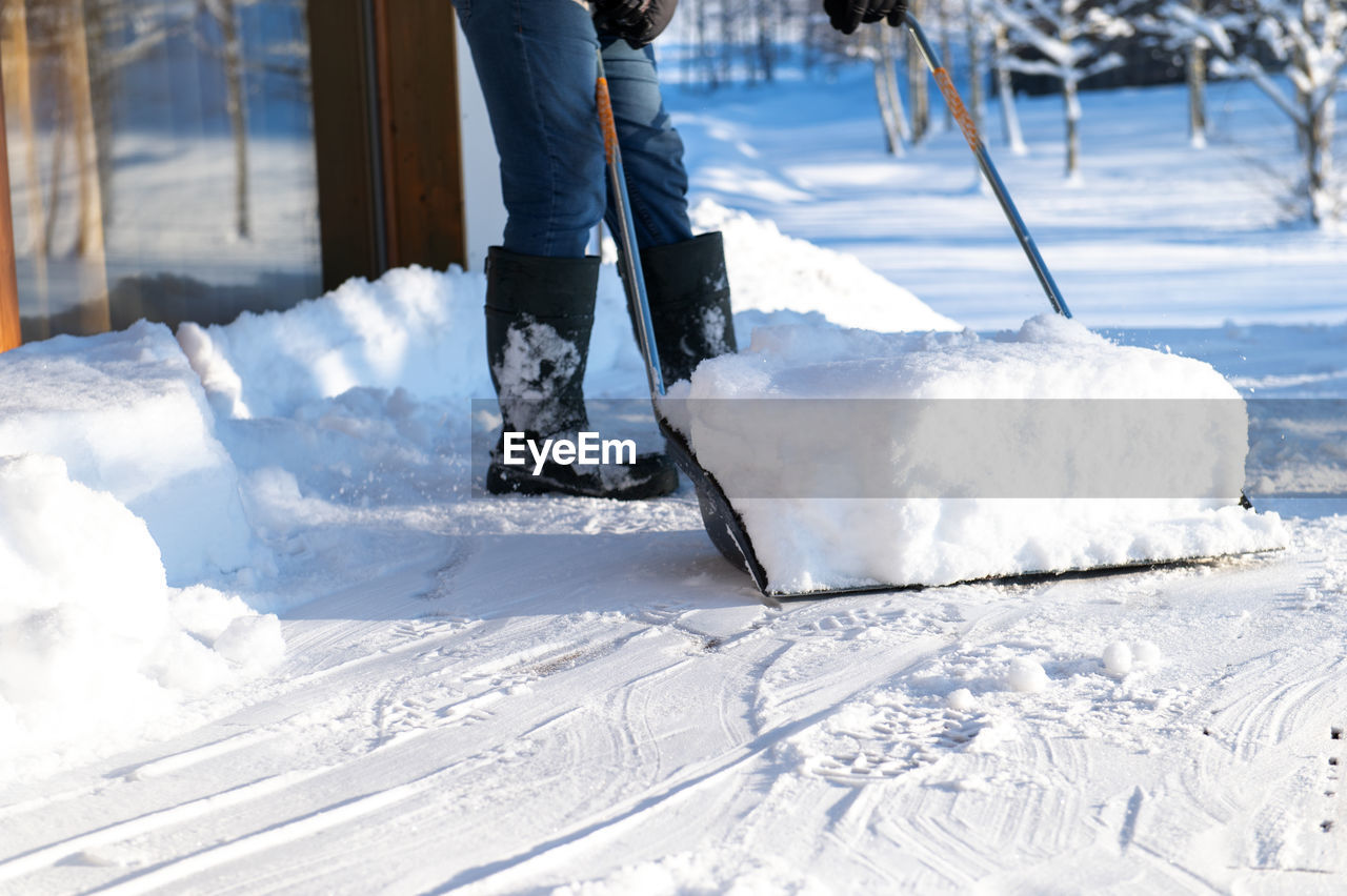 A man in rubber boots with a snow shovel cleans the snow from the terrace of the house