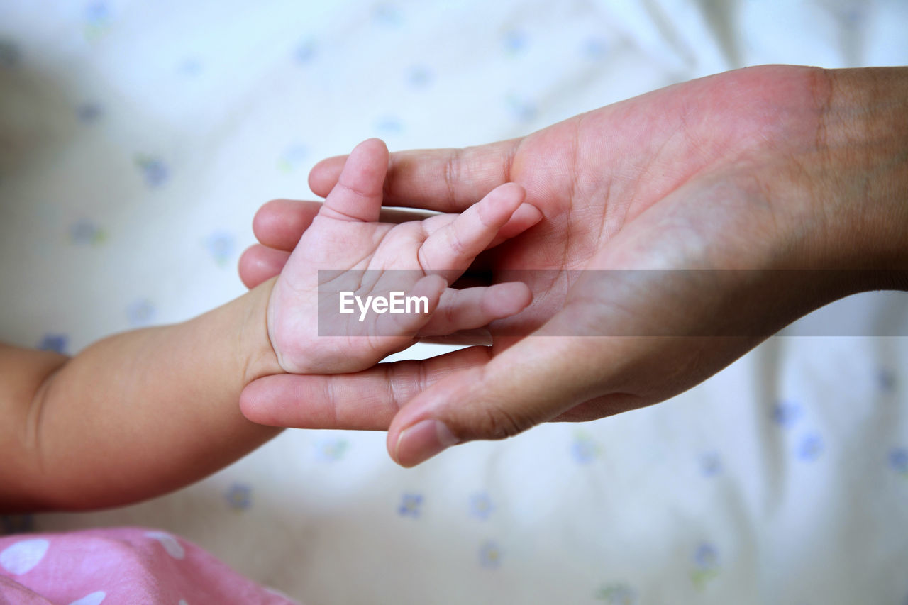 Cropped image of mother holding baby hand on bed at home