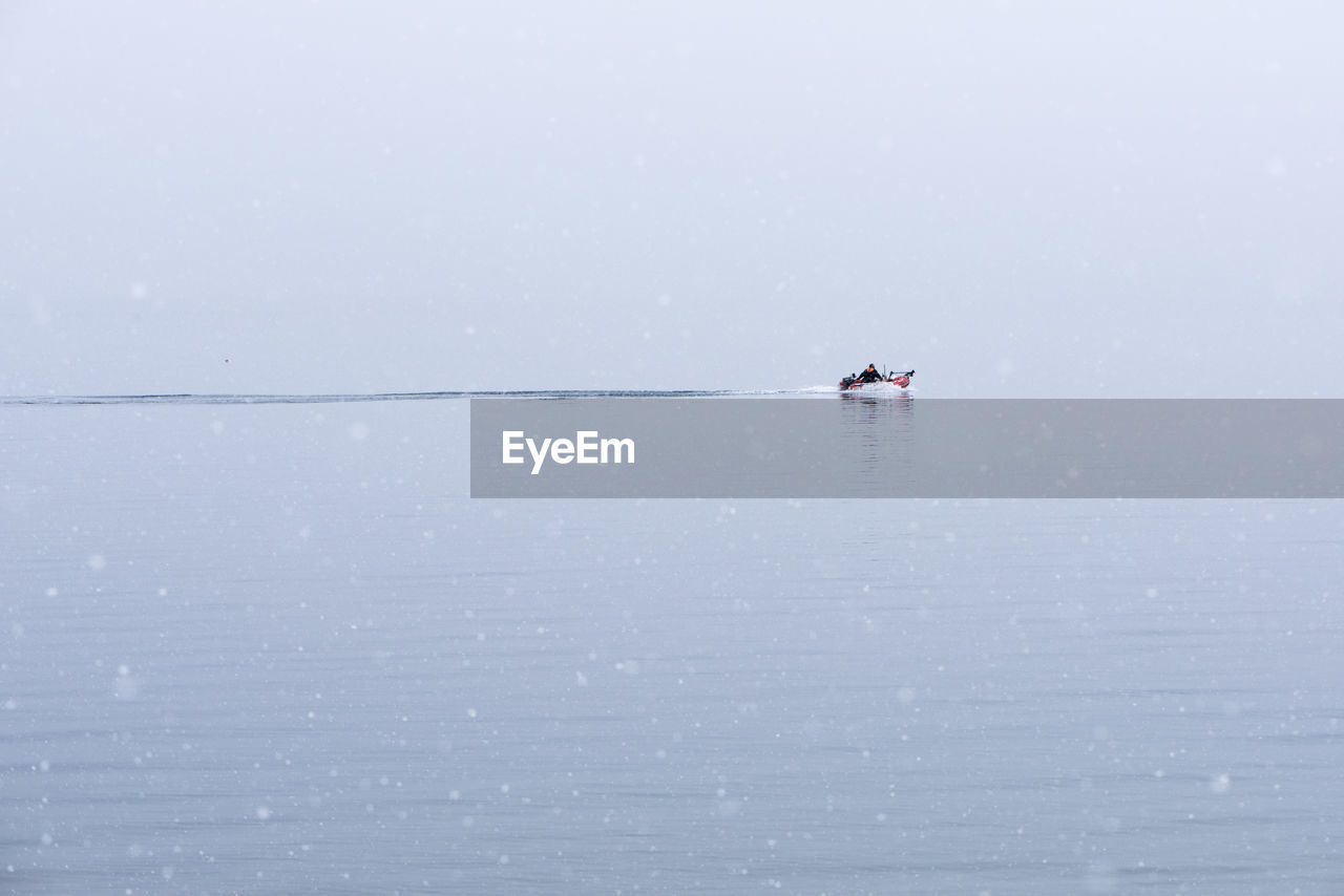 Person on motorboat in sea against clear sky during snowfall