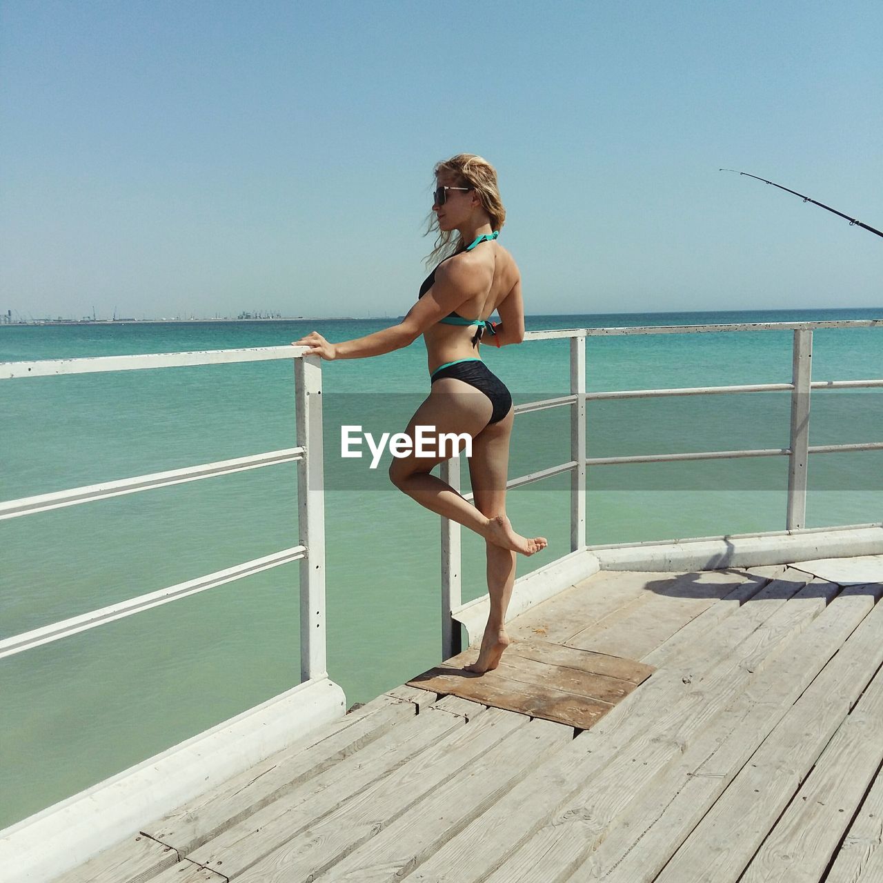 Side view of seductive woman standing by railing on boat against clear sky during sunny day