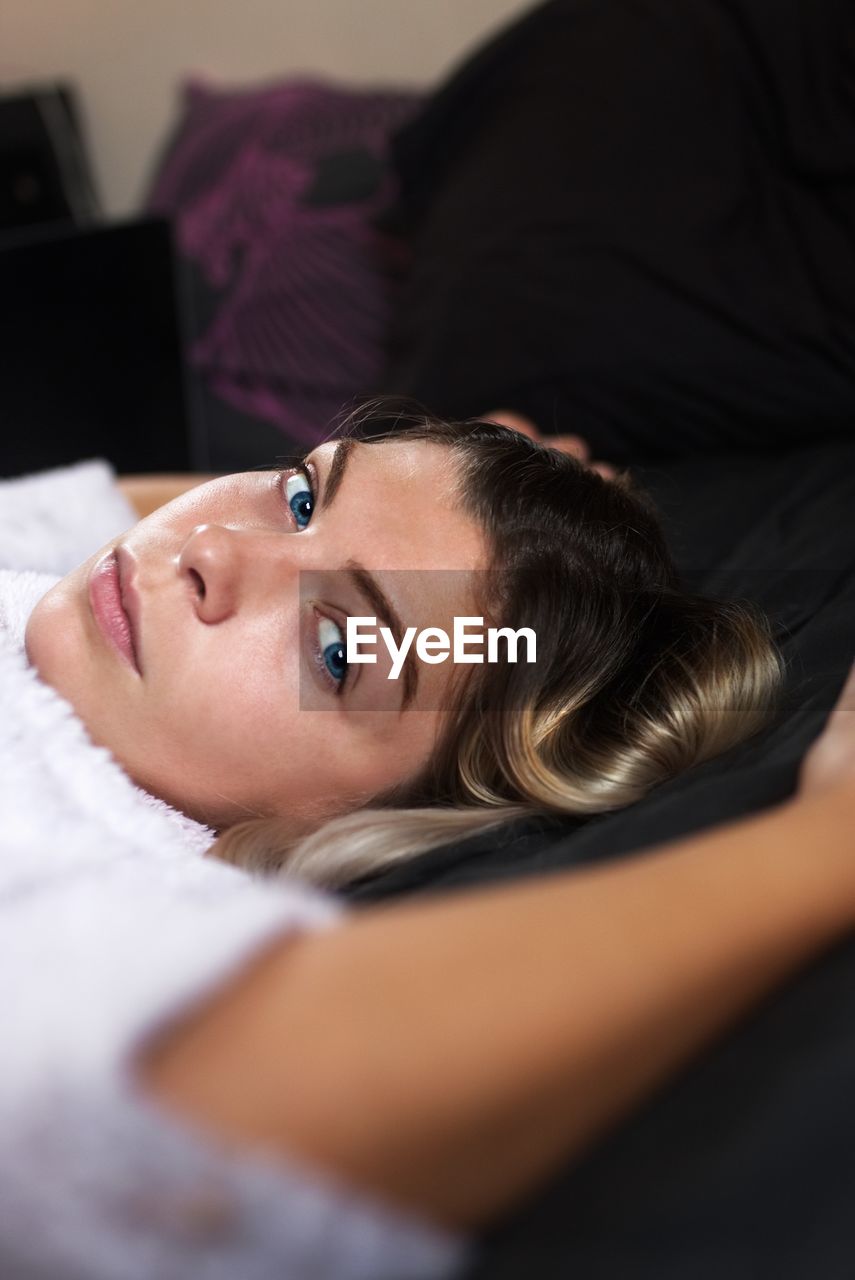 Close-up portrait of young woman lying on bed at home