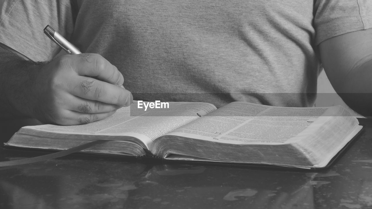 Midsection of man writing on book