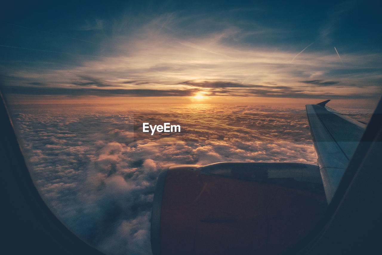 Cropped image of airplane flying over cloudscape against sky seen through window