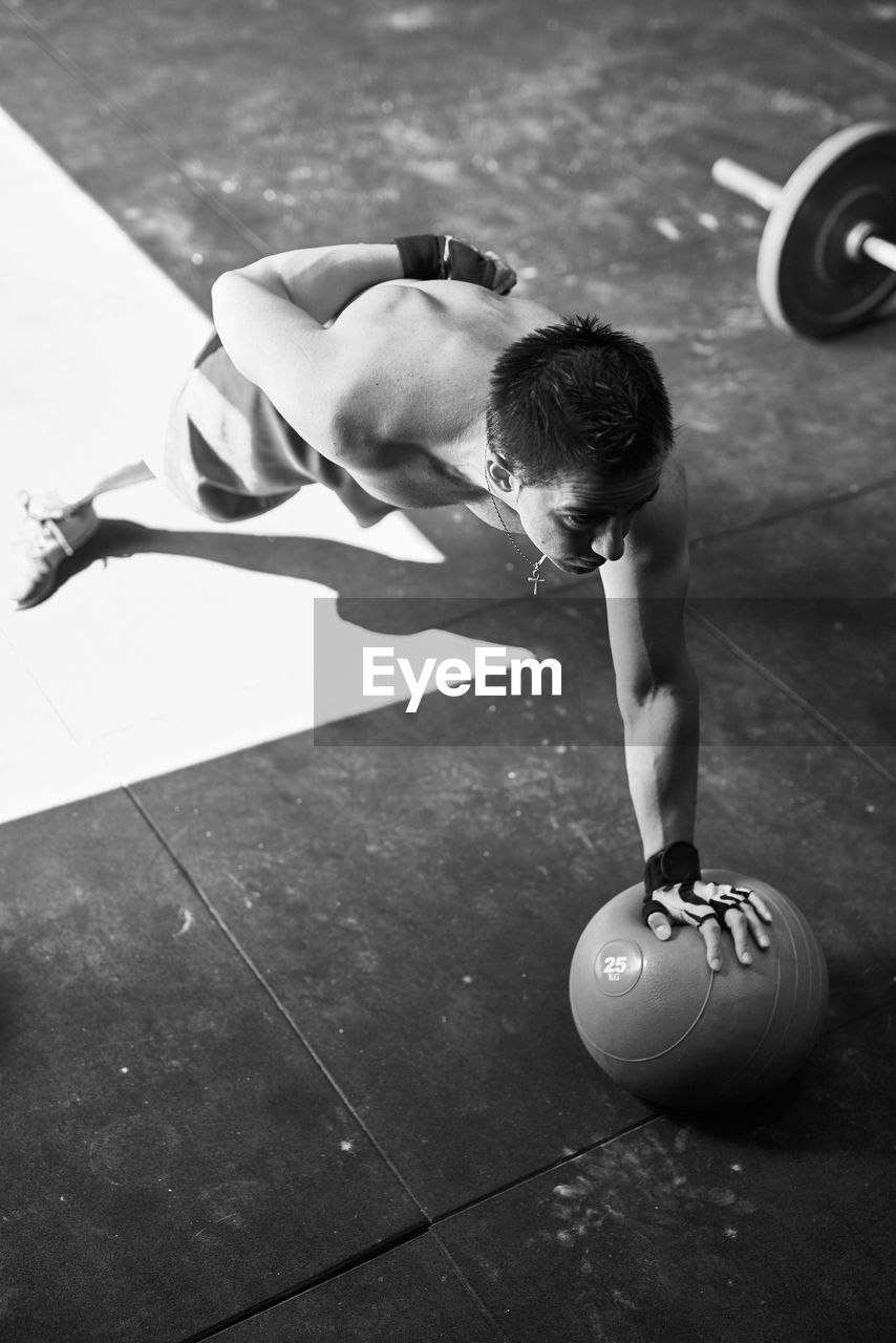 Shirtless fit young man doing one hand push up with a heavy ball