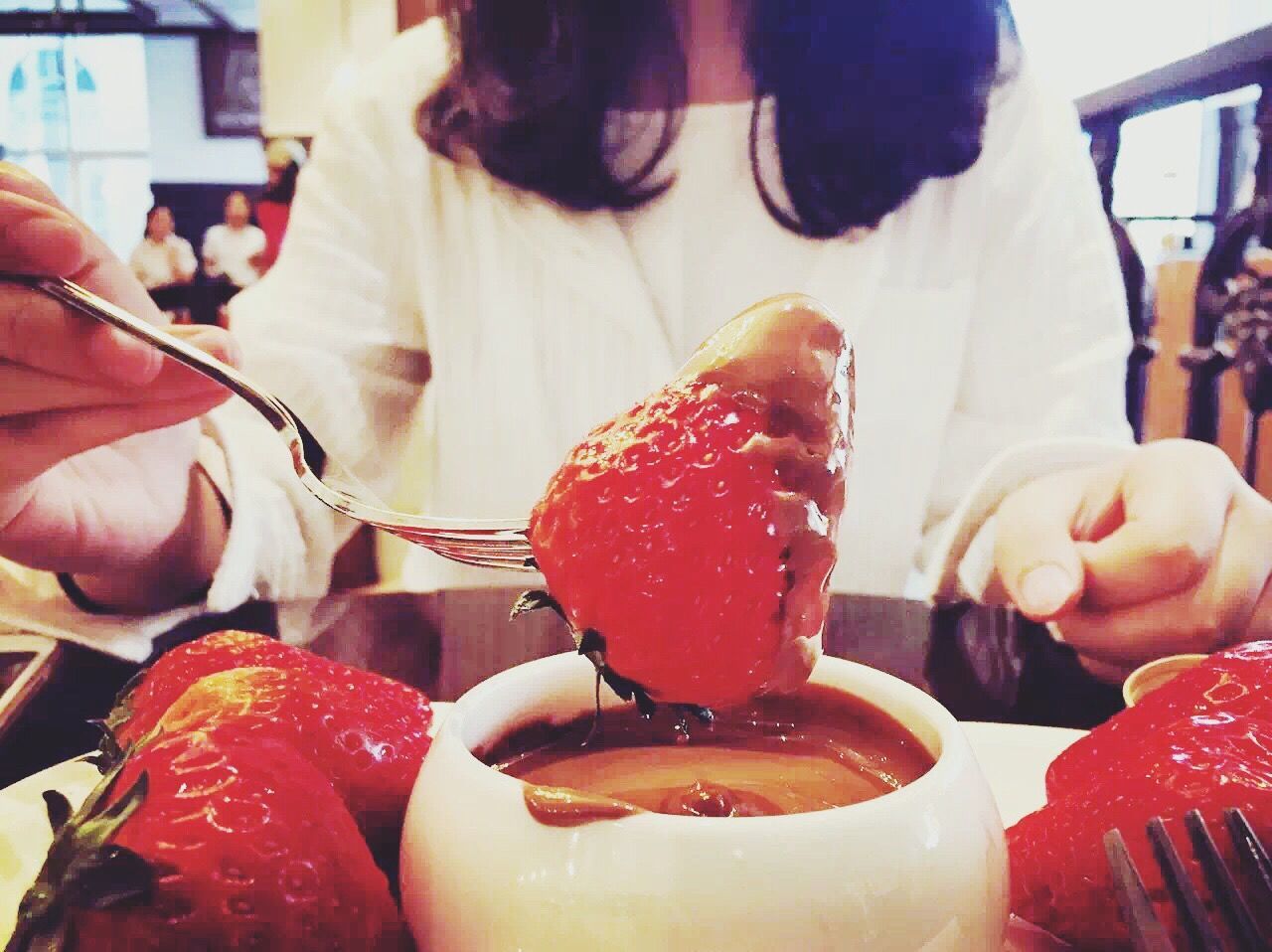 Close-up of woman eating strawberry with chocolate syrup at restaurant