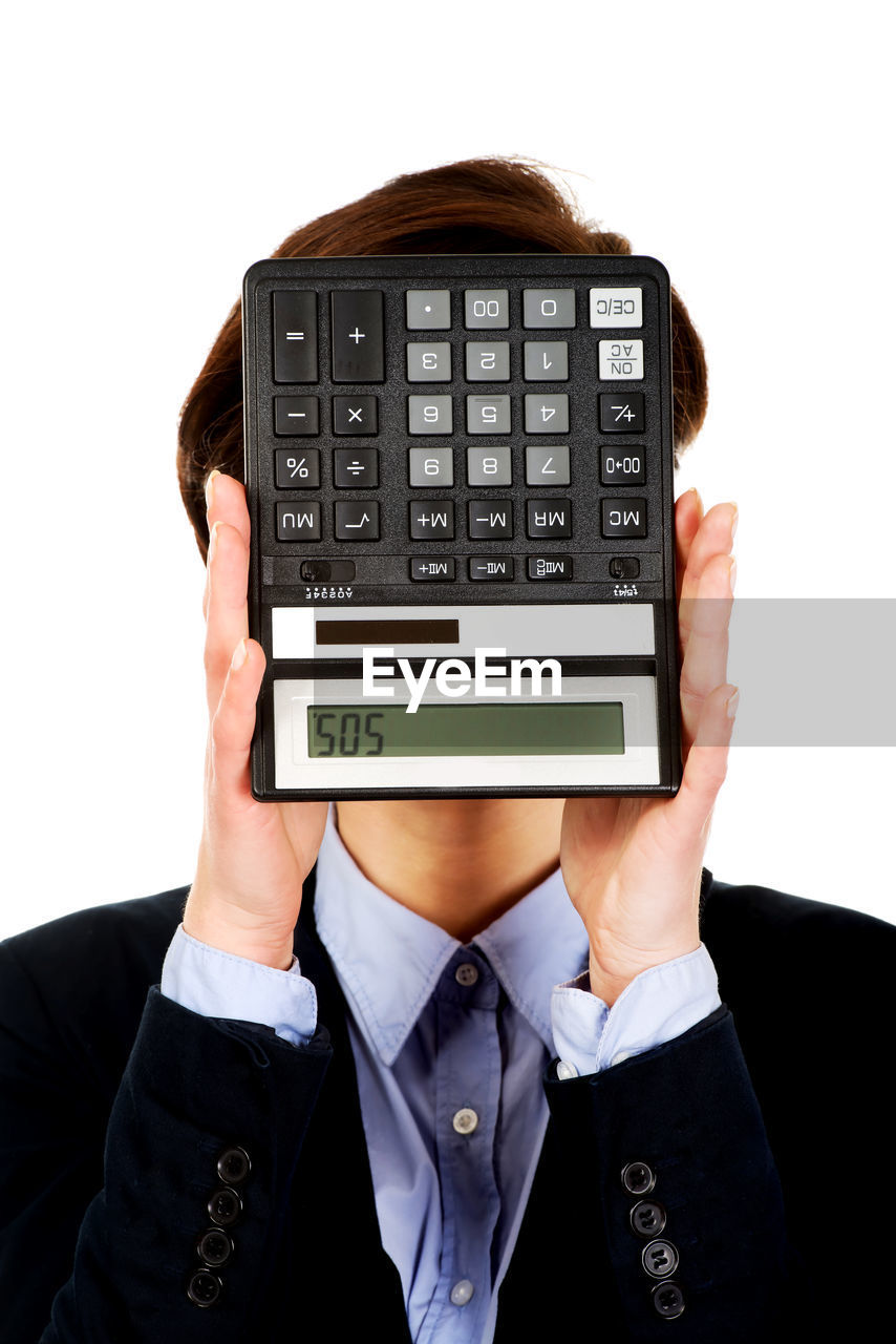 Close-up of businesswoman holding calculator over face against white background