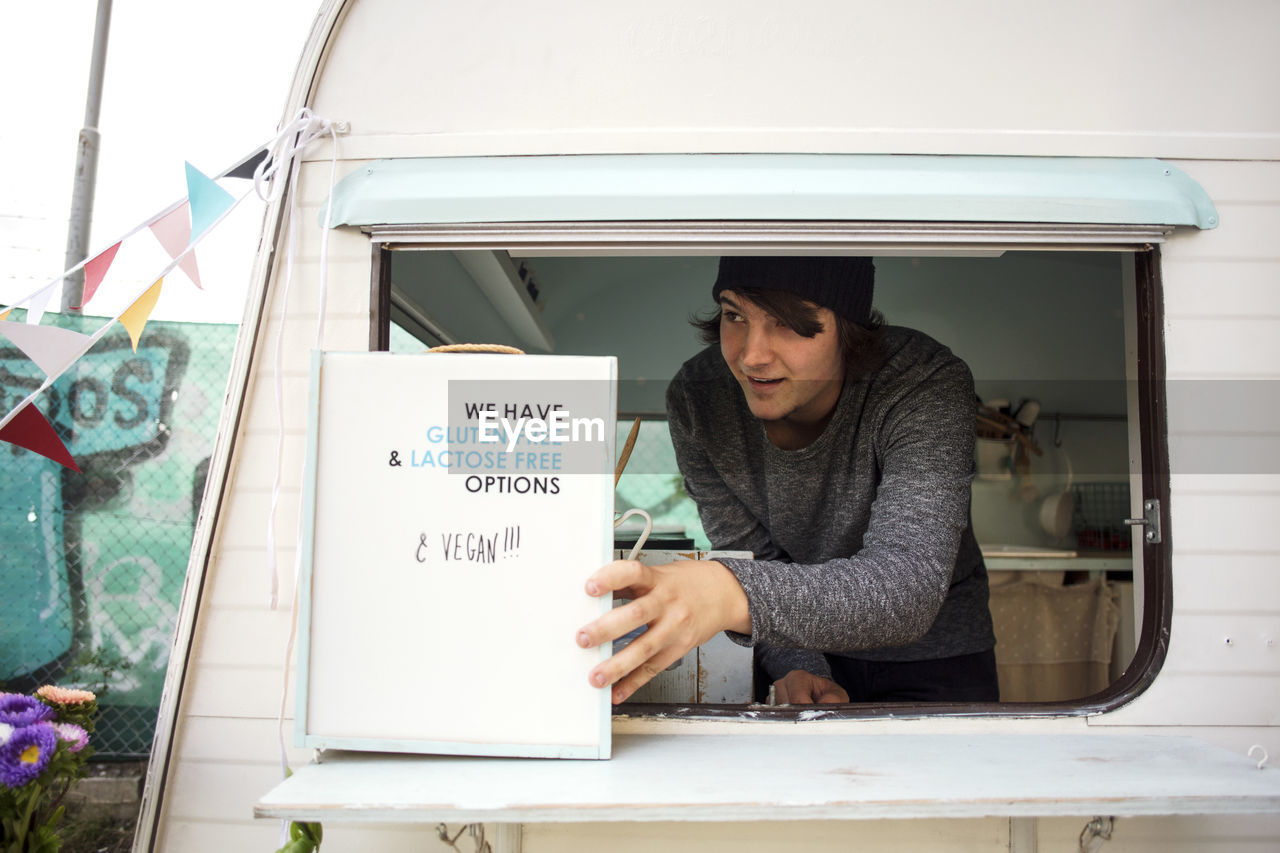 Male owner looking away while placing sign at window on food truck