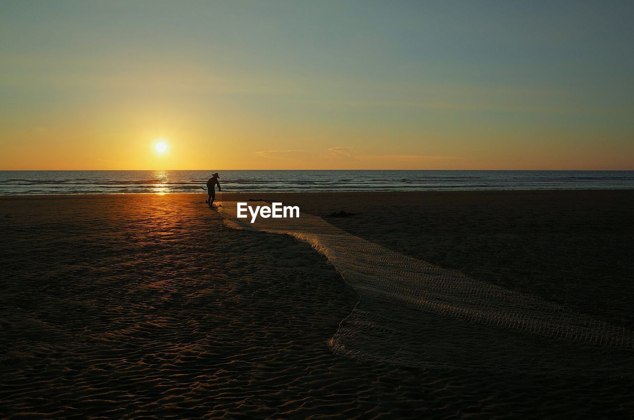 Man with fishing net on beach at dusk