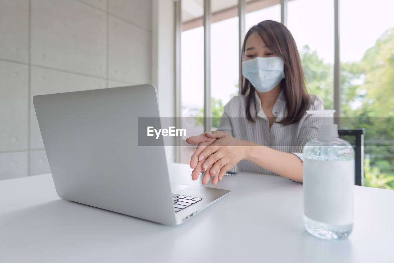 Young woman using sanitizer while sitting on table