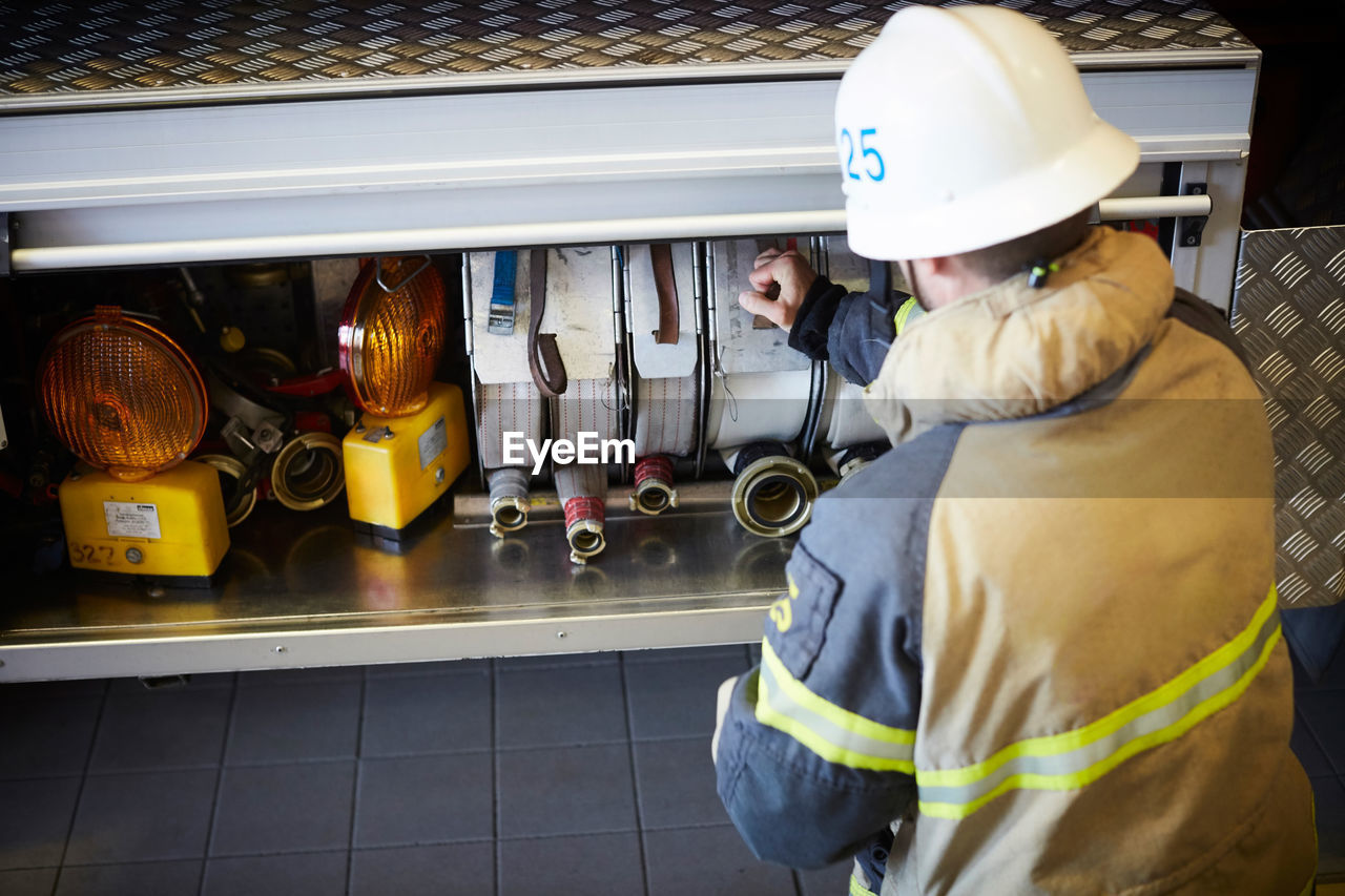 Rear view of firefighter arranging fire hose in engine at fire station