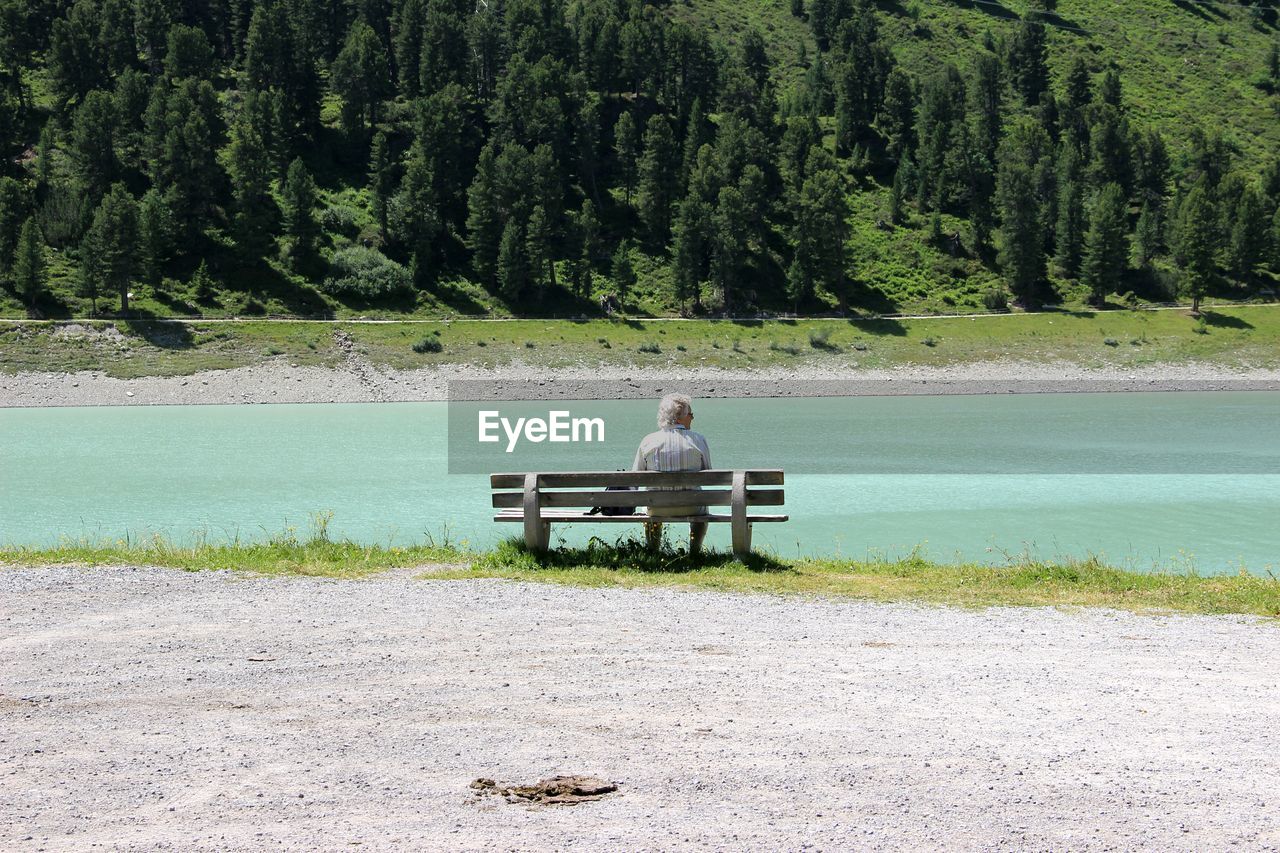 REAR VIEW OF PEOPLE SITTING ON LAKE