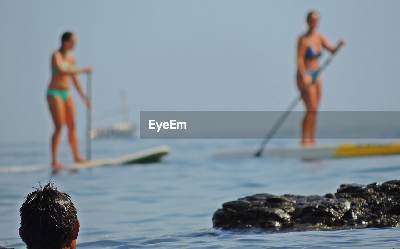 Rear view of man looking at women in biking paddleboarding on sea