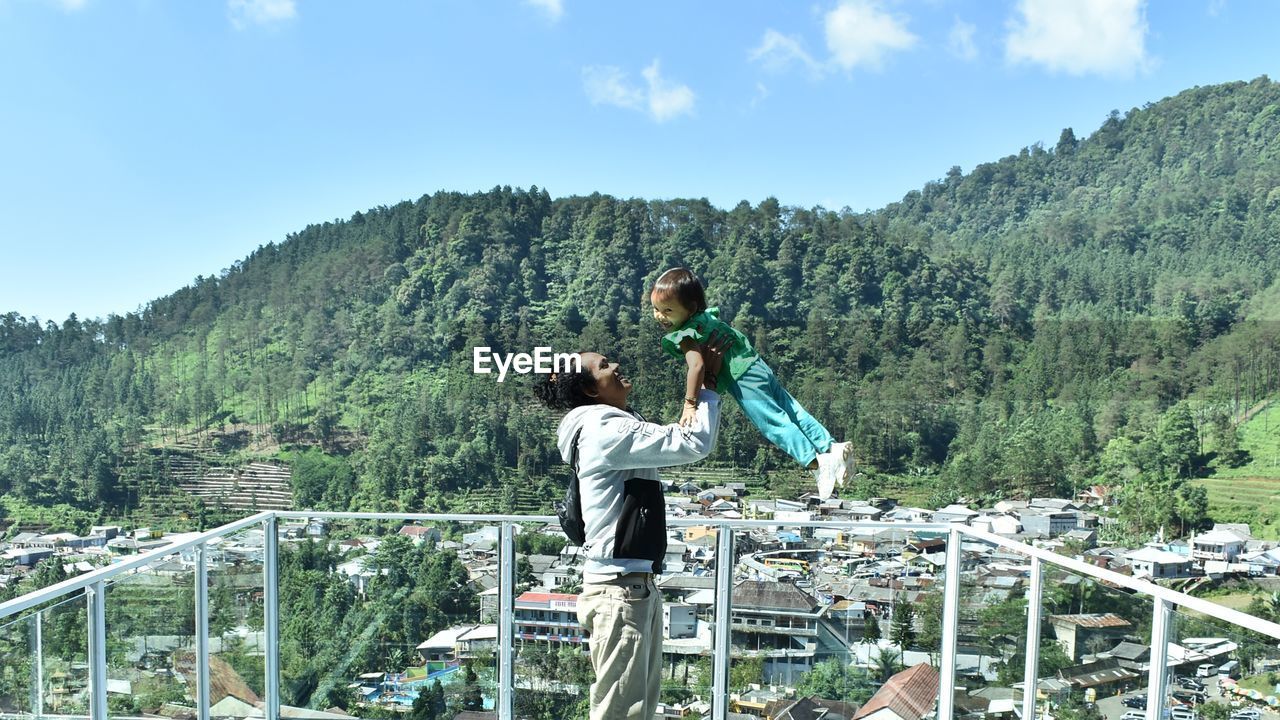 REAR VIEW OF MAN AND WOMAN STANDING ON MOUNTAIN AGAINST SKY