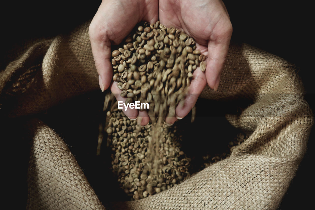 Close-up of cupped hands holding raw coffee beans over burlap sack