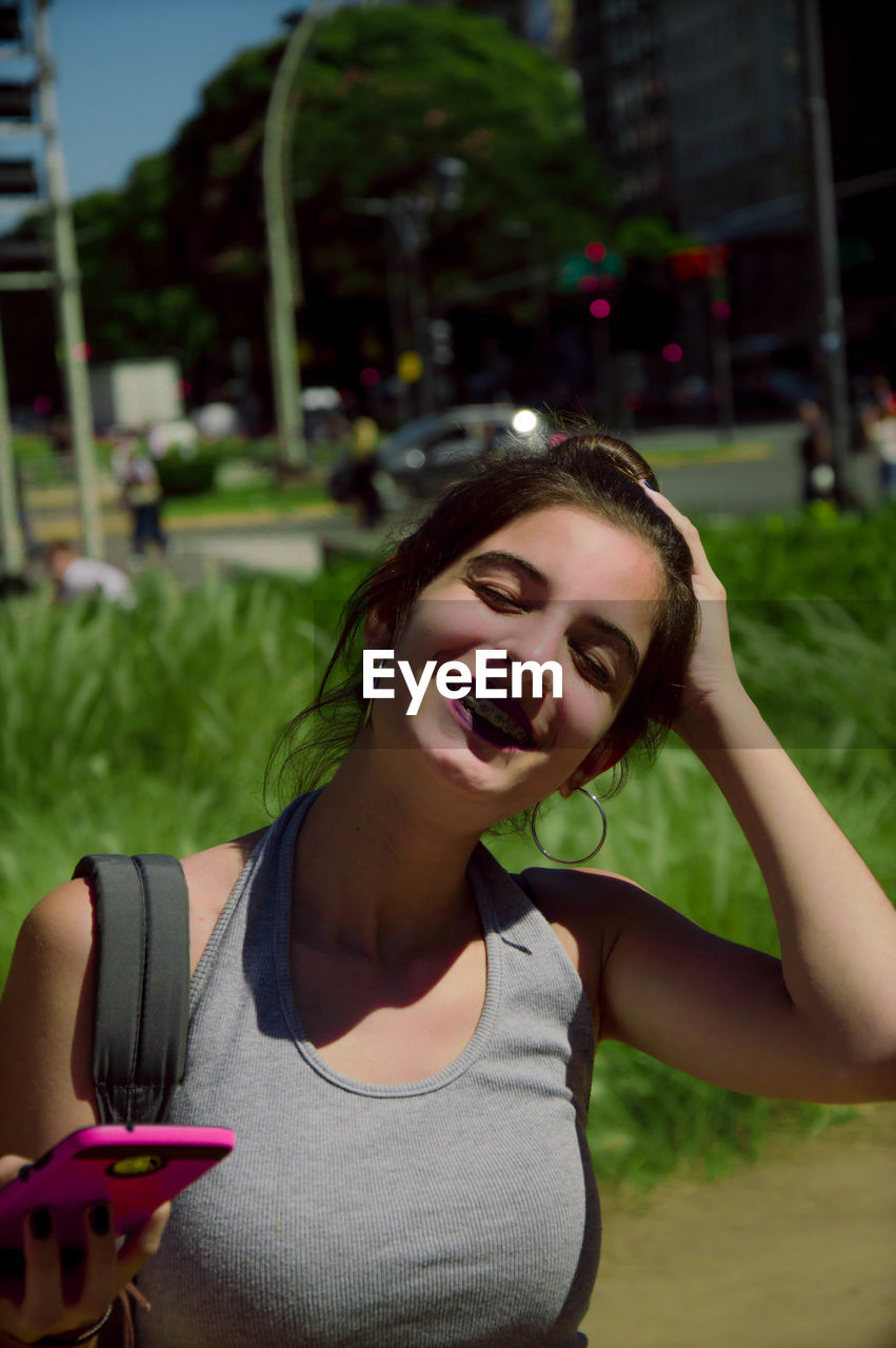 Smiling young woman with eyes closed standing against plants