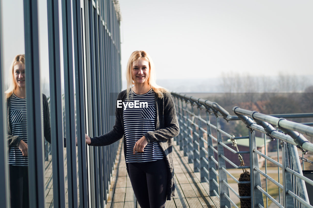 Portrait of young woman standing by railing in city