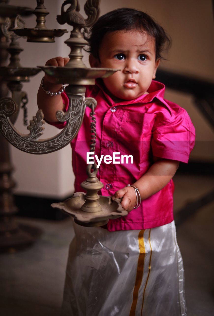 Baby girl wearing traditional clothing standing by diya