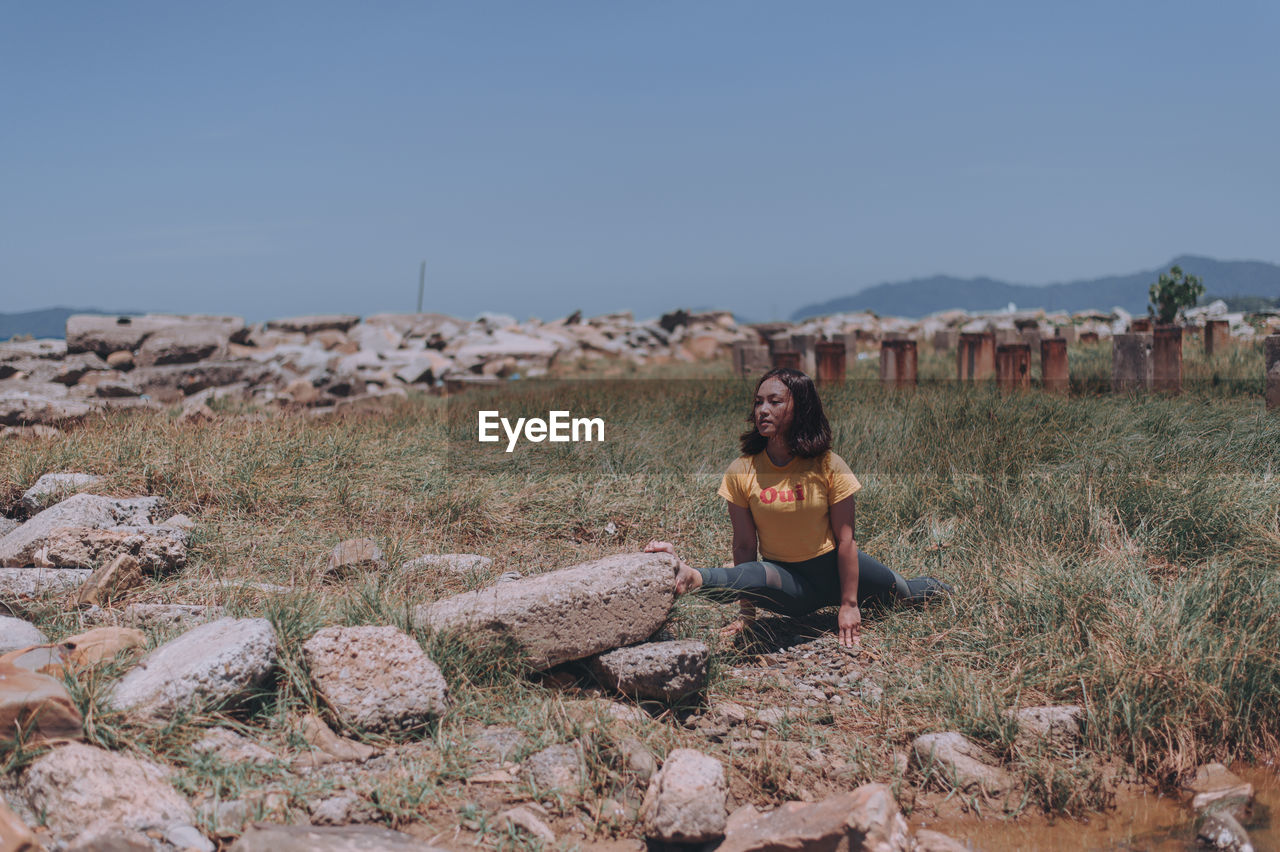 Young woman exercising on grassy land against clear sky