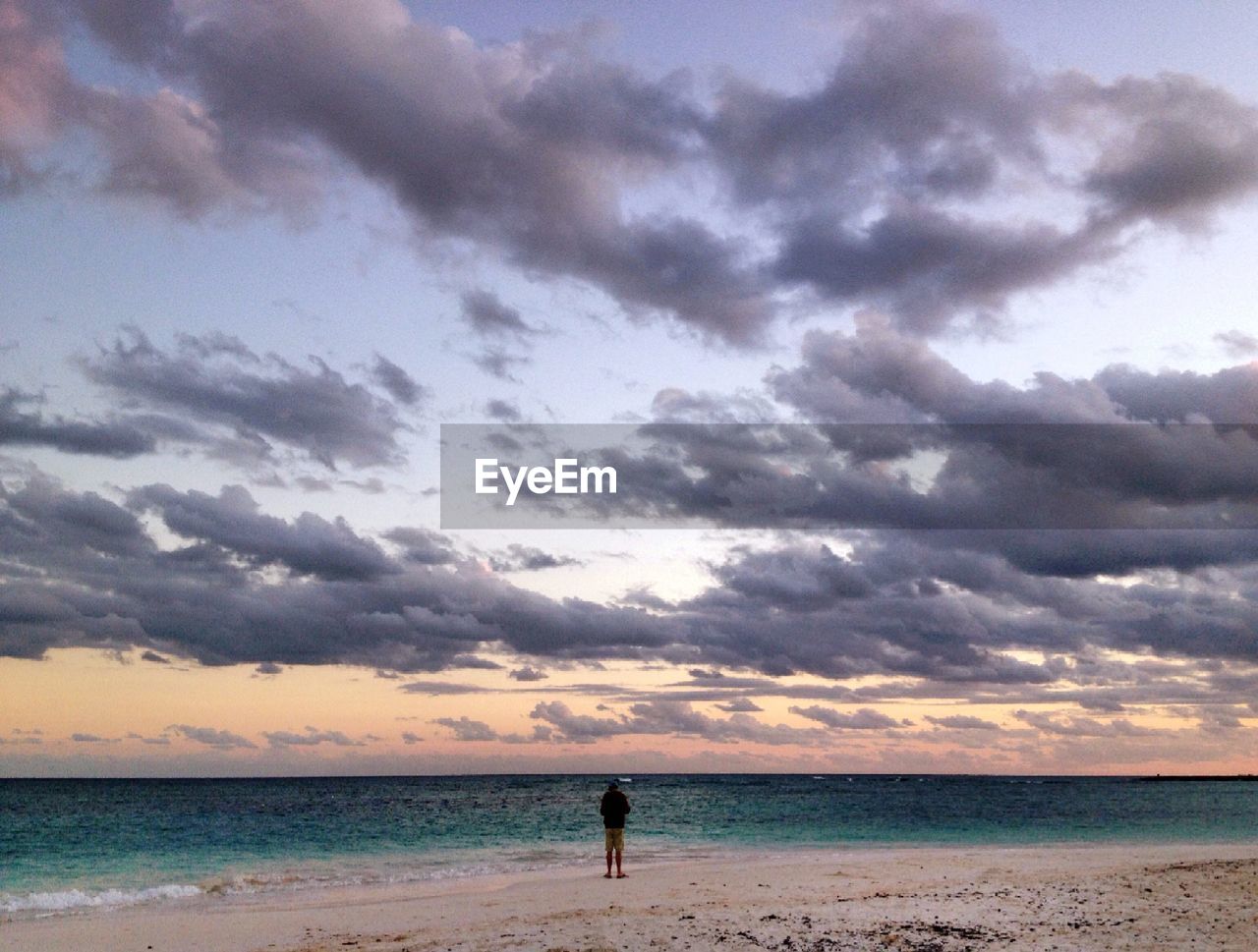 Rear view of man standing at beach against cloudy sky