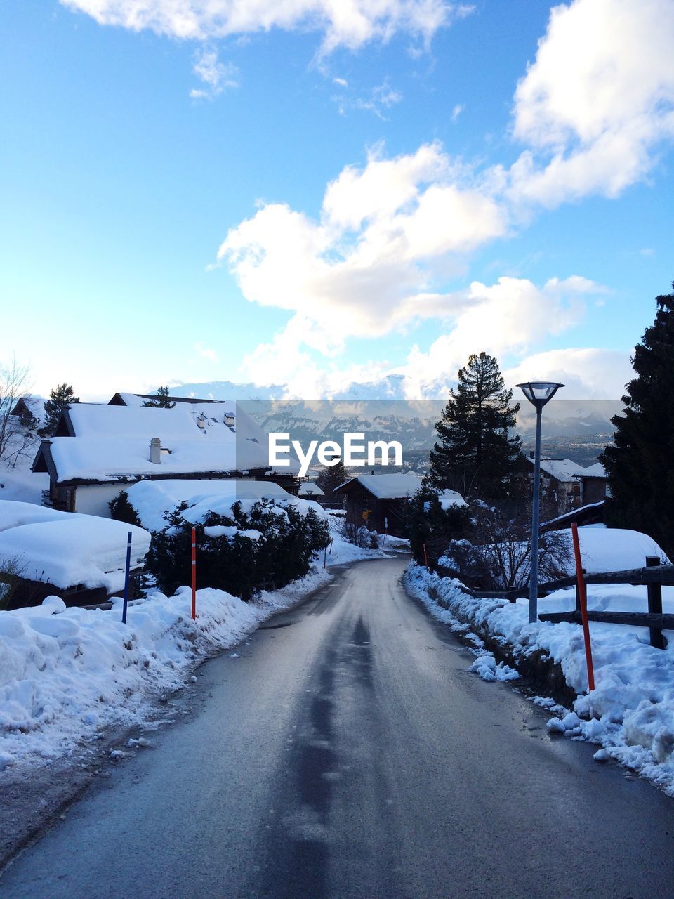 Empty road by snow covered houses against sky